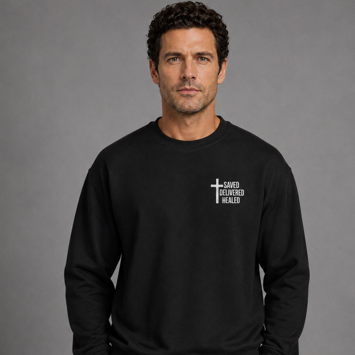 Man wearing black Saved Delivered Healed embroidered crew neck sweatshirt, front view close-up of chest embroidery