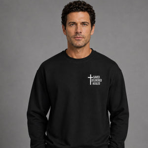 Man wearing black Saved Delivered Healed embroidered crew neck sweatshirt, front view close-up of chest embroidery