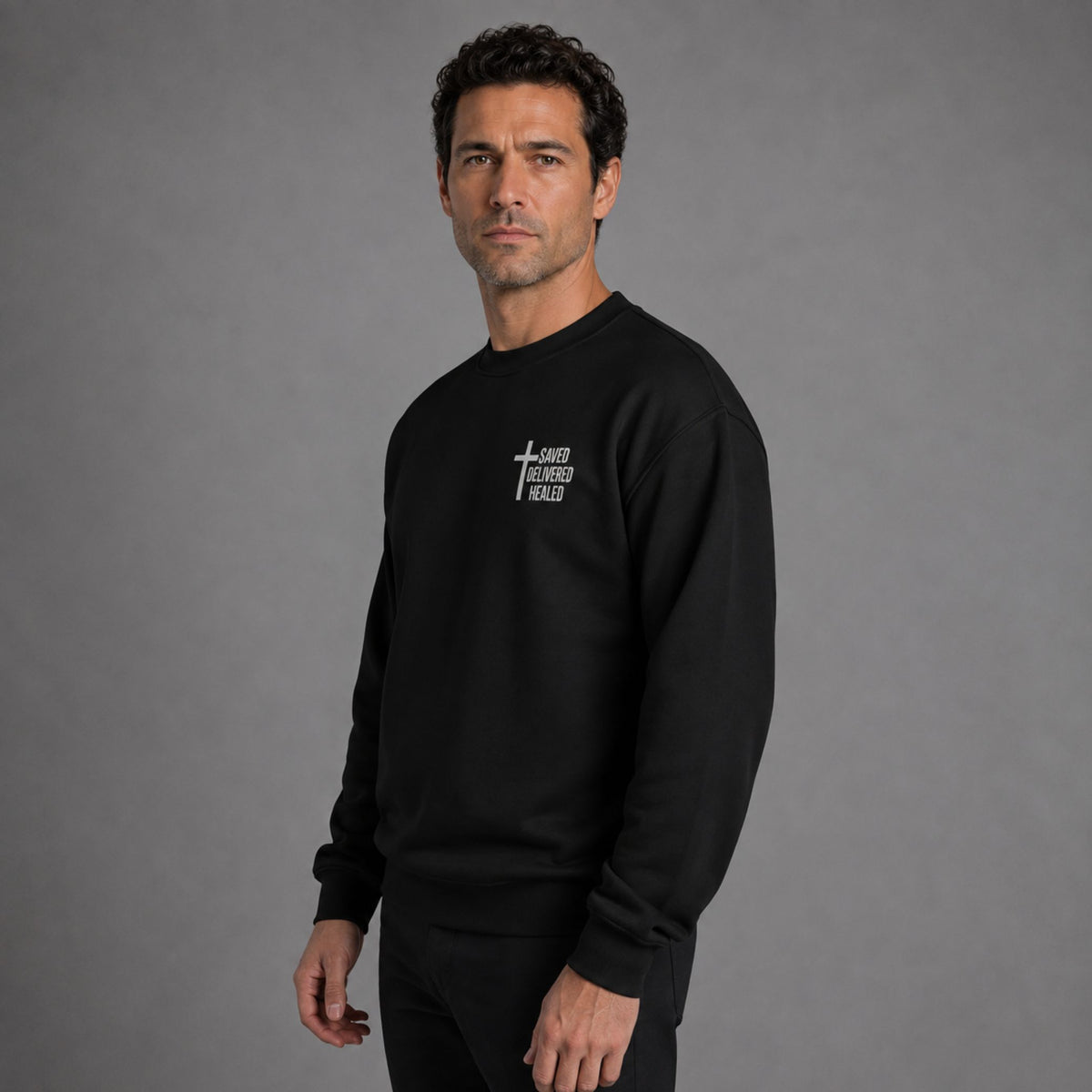 Man modeling black Saved Delivered Healed embroidered crew neck sweatshirt, three-quarter side view