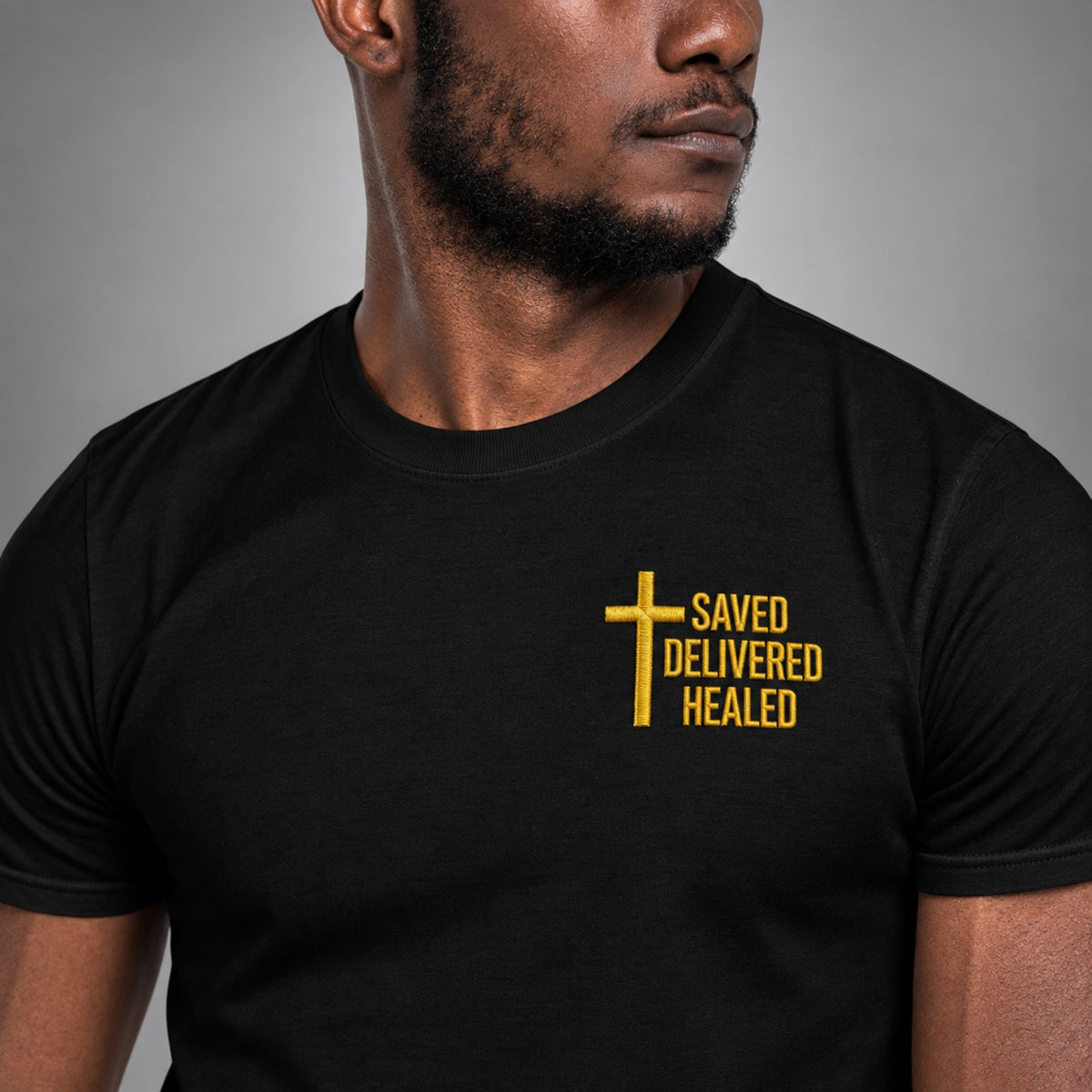 Close-up of gold embroidered Saved Delivered Healed cross on a black Full Salvation Apparel t-shirt