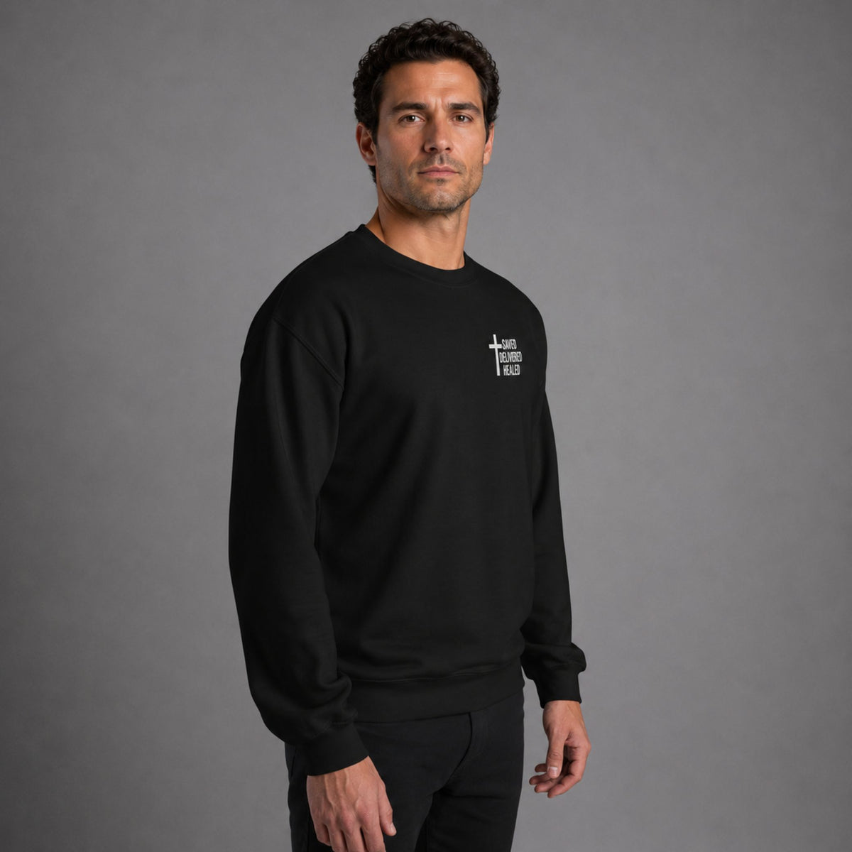 Full body side view of man wearing black Saved Delivered Healed embroidered crew neck sweatshirt