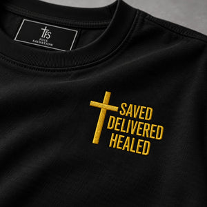 Macro detail of the gold embroidered cross and Saved Delivered Healed lettering on black cotton