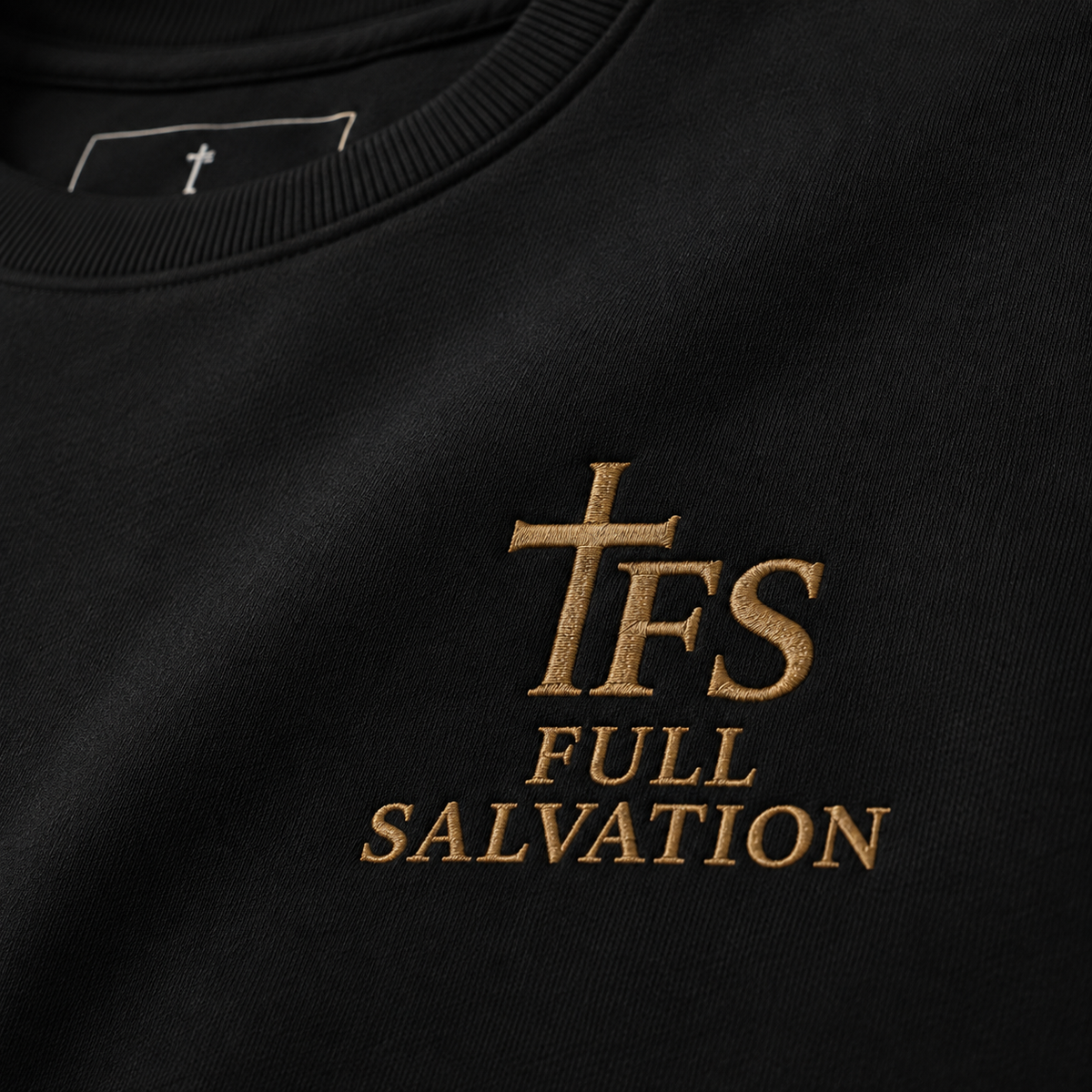Macro detail of the 2x2 rib collar, self-fabric neck tape, and embroidered Full Salvation cross emblem on the Essential Organic Cotton Crewneck Sweatshirt in Black