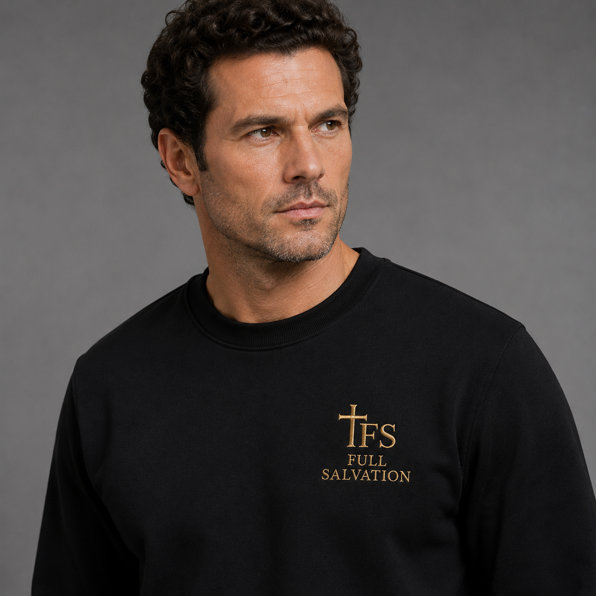 Man wearing the Full Salvation Apparel Essential Organic Cotton Crewneck Sweatshirt in Black, close-up of the embroidered gold cross emblem at the chest